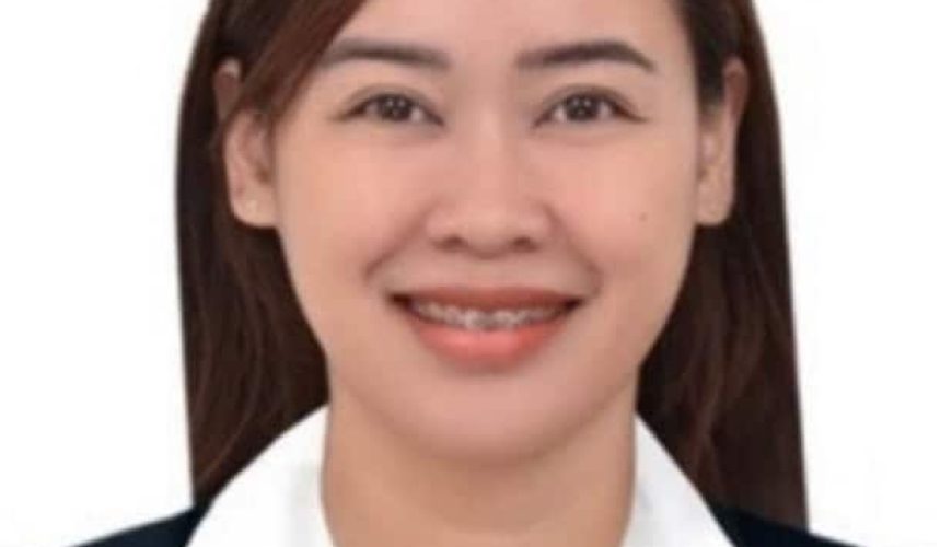 A woman with straight brown hair, wearing a black blazer and white collared shirt, smiling at the camera against a plain white background.