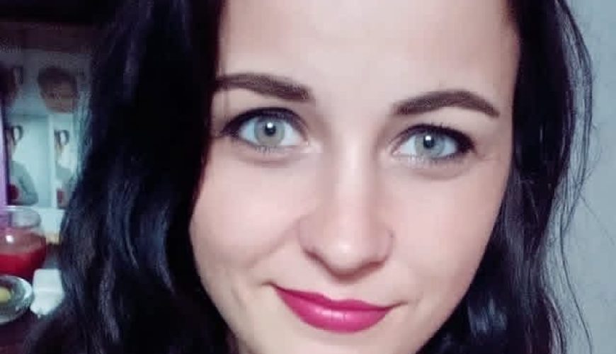 Į kamerą šypsosi ilgų, banguojančių tamsių plaukų ir mėlynų akių moteris. Ji vilki rausvą palaidinę ir atrodo esanti patalpoje.